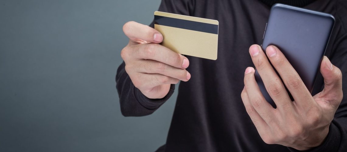 Thieves wear a black hat, hold the phone and a smart card on a gray background.